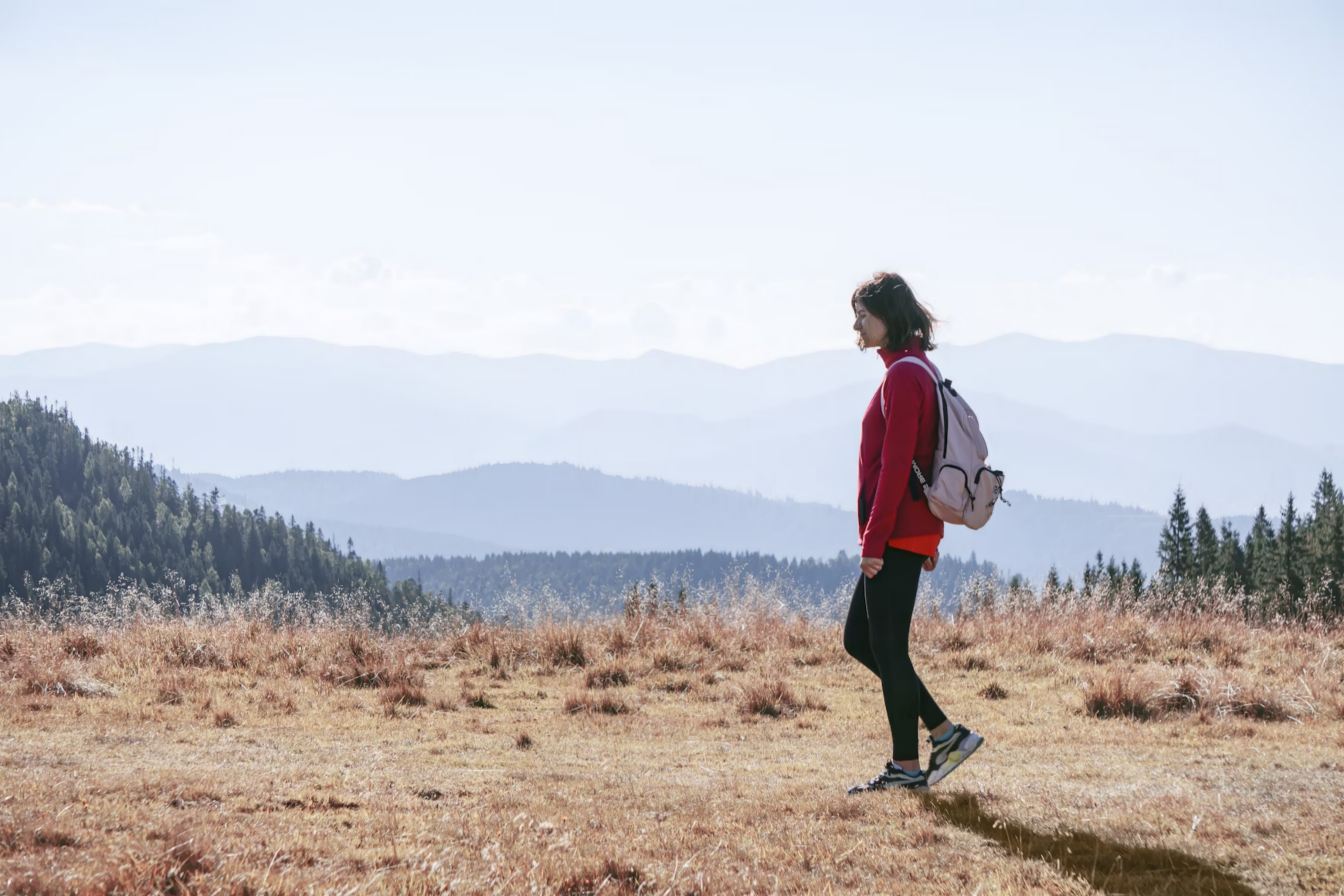 3. A woman with a backpack stands on a hill, overlooking the vast landscape in the distance.
